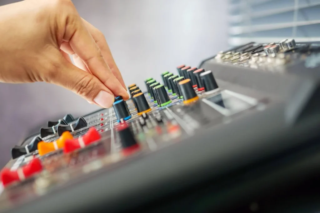 A close-up of a person’s hand adjusting a multi-colored rotary knob on an audio mixing console, which functions as a potentiometer to provide seamless analog control and tactile precision necessary for professional audio mixing.