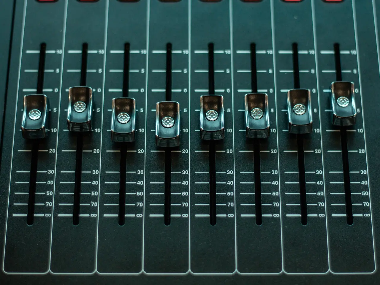Row of slide potentiometer faders on an audio mixing console.